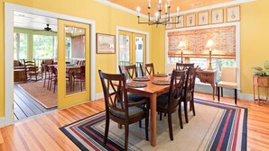 A dining area with a wooden table and chairs, a chandelier, and framed artwork on the walls. - Blue Skies | Game Room, Fire Pit & More! (Tybee Island)