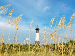 A lighthouse with a white and black structure, surrounded by tall grass and a clear blue sky.