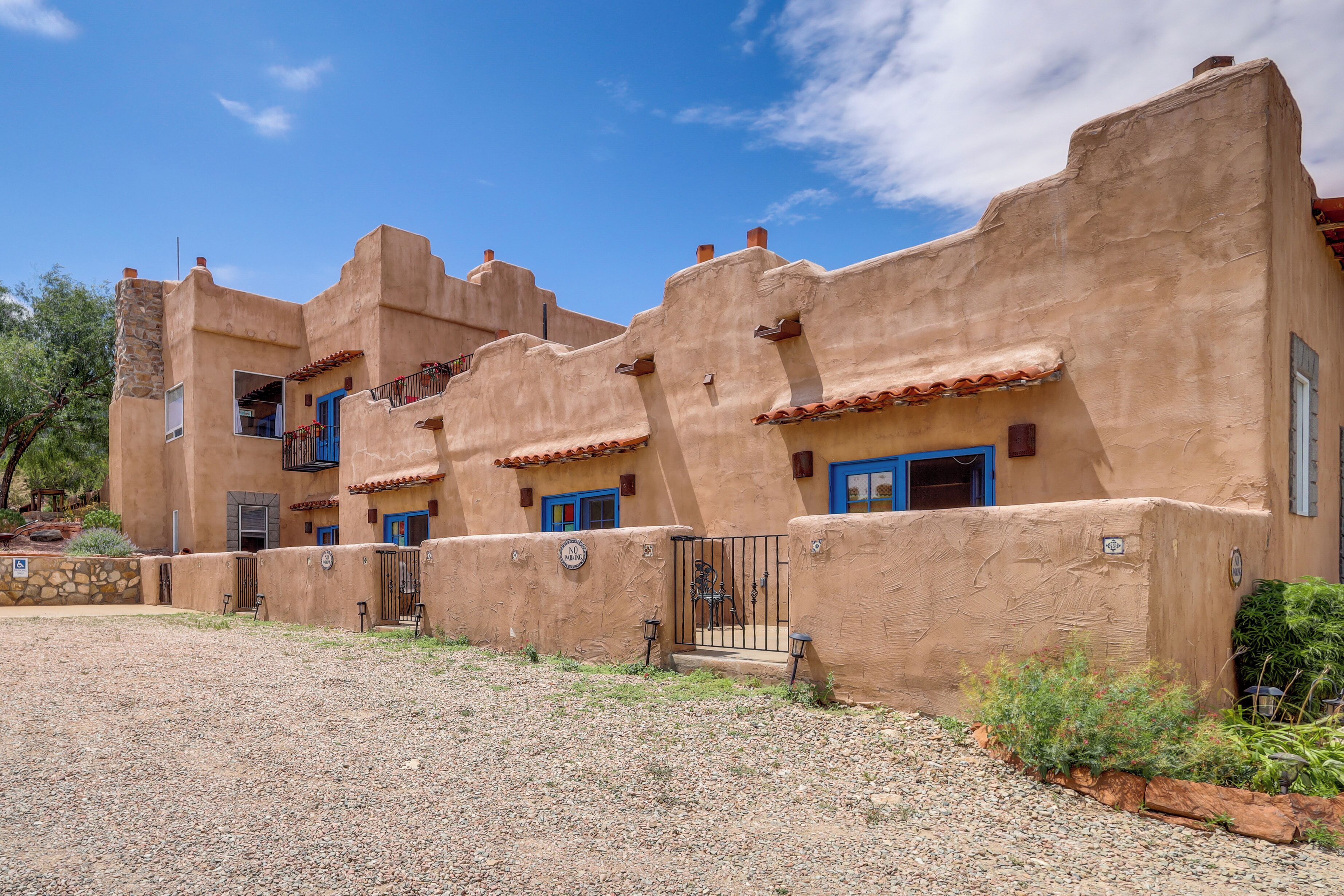 A building with stucco walls and blue doors, featuring a gravel driveway and a small garden area.
