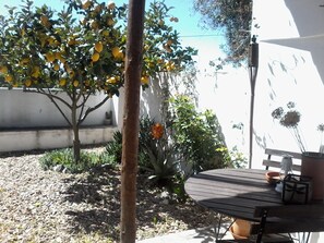 A patio area with a round wooden table, potted plants, and a tree bearing yellow fruits. -  Tia Luísa Cottage (country house) (Redondo)
