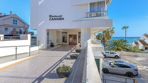 Een modern hotel met vrij uitzicht op zee, een overdekte ingang en een parkeerplaats met auto's.