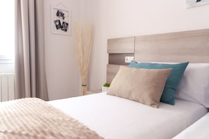 A neatly made bed with a beige and teal pillow, a white headboard, and a wall-mounted photo frame.