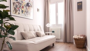 Een moderne woonkamer met een witte bank, een groot abstract schilderij, een radiator, een raam met gordijnen, en een rieten mand.