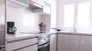 Een moderne keuken met witte kasten, een inbouwoven, een koffiezetapparaat en een raam dat zorgt voor natuurlijk licht.
