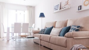 Een moderne woonkamer met een beige bank, een glazen salontafel en een eethoek met witte stoelen.