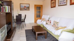 Ein Wohnzimmer mit Sofa, Couchtisch, Fernseher, Bücherregal und Essbereich.