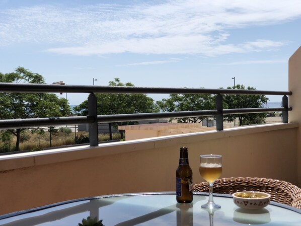 A balcony with a table, a bottle, and a glass of beer, overlooking a coastal area with trees and buildings.