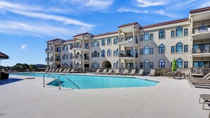 Un hotel de varios pisos con piscina, mobiliario exterior y balcones.