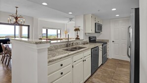 Una cocina moderna con armarios blancos, encimeras de granito, lavavajillas integrado y un refrigerador de acero inoxidable.