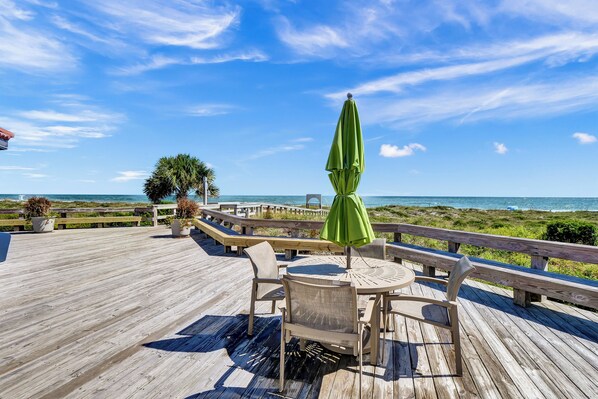 Eine Holzterrasse mit Tisch und Stühlen mit Blick auf einen Strand und einem klaren Himmel.