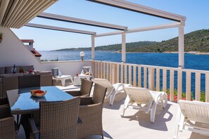 A terrace with wicker furniture, a table with fruit, and a view of the sea.