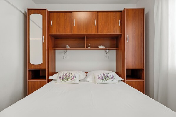 A bedroom with a bed, two pillows, a nightstand, a mirror, and wooden wardrobe with multiple compartments.