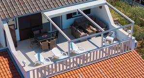 A two-story building with a balcony, outdoor seating area, and a tiled roof.