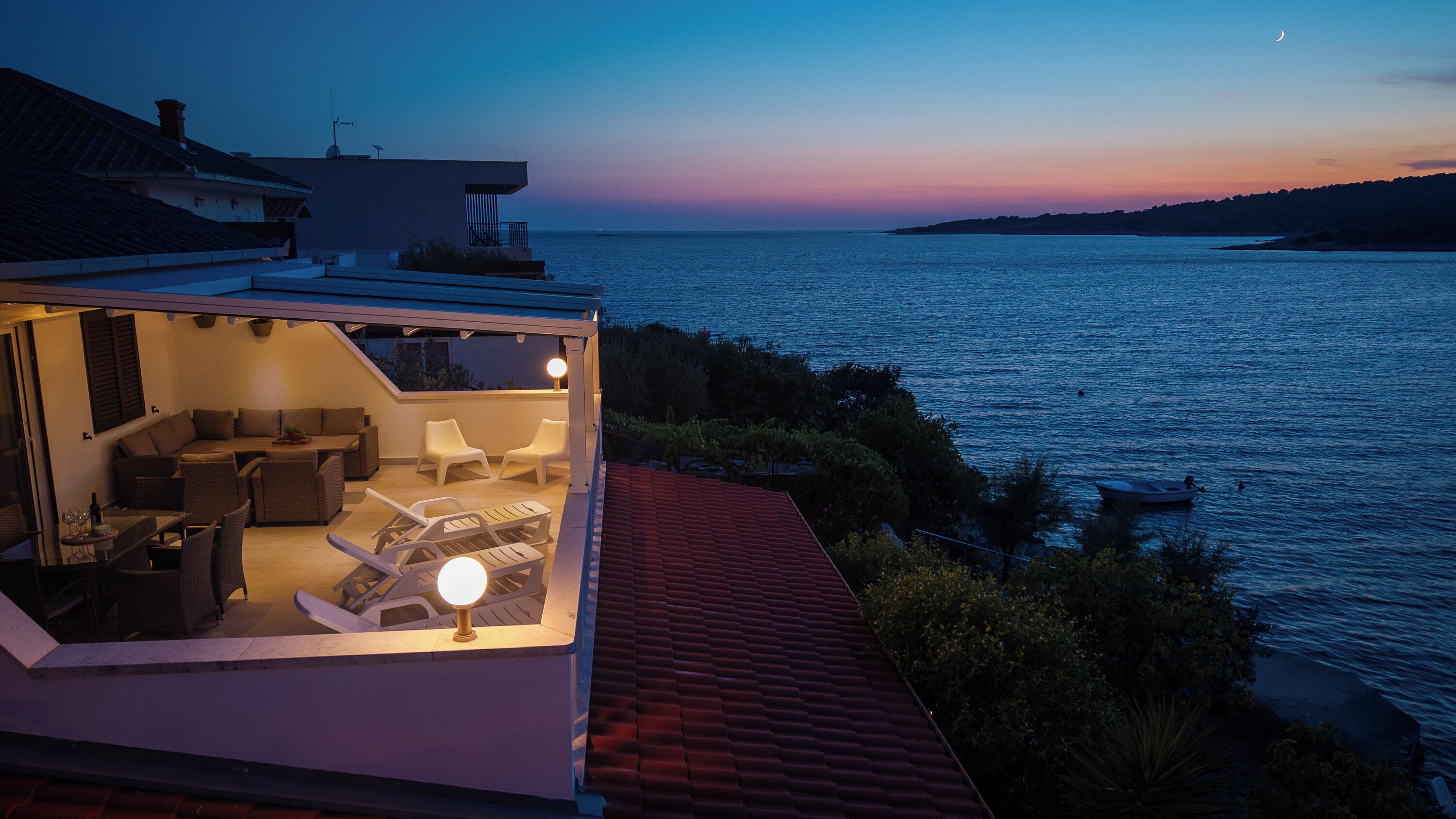 A modern outdoor living space with a pool, lounge chairs, and a view of the sea at dusk.