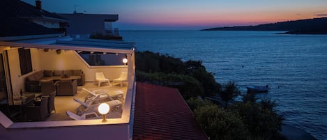 Ein moderner Außenbereich mit Pool, Liegestühlen und Blick auf das Meer bei Einbruch der Dämmerung.