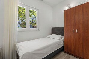 Un lit simple avec un matelas et un oreiller blancs, une armoire en bois et une fenêtre donnant sur un paysage verdoyant.
