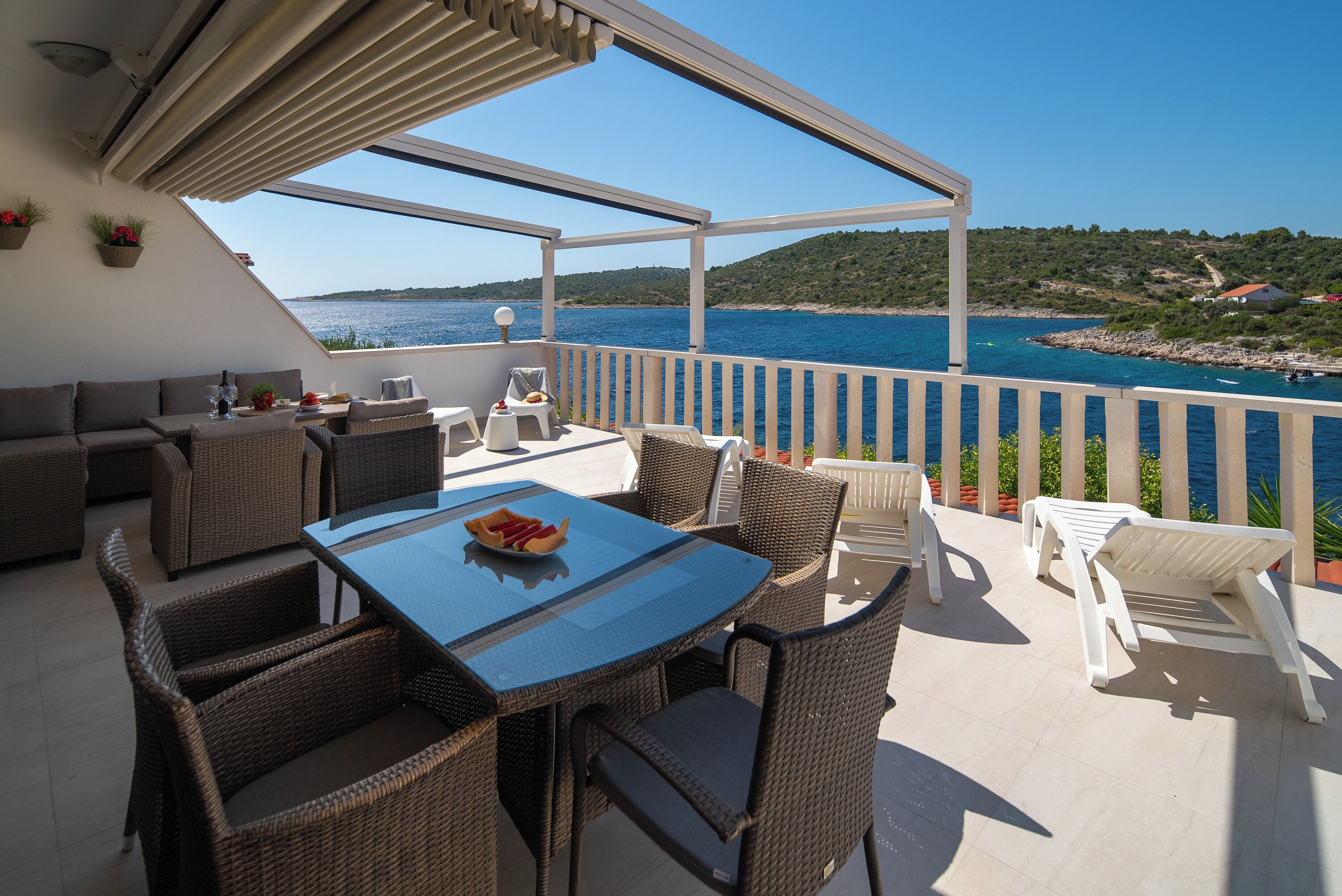 A terrace with wicker furniture, a glass table, and a view of the sea.