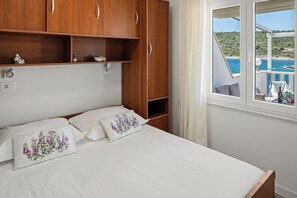 A bedroom with a bed, wooden wardrobe, and a window with a view of the sea.