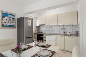 A modern kitchen with a built-in oven, a stainless steel refrigerator, and a dining area set with plates, glasses, and a vase of flowers. - Apartment Bose 6+0 with big balcony and sea view only 5 meters from beach  (Dvornice, Rogoznica)