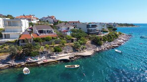 A coastal residential area with houses, a clear blue sea, and boats.