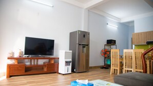 A living room with a flat-screen TV, a refrigerator, wooden chairs, and a table with a tissue box. - 3BR bedroom house near the beach and golf course  (Da Nang)