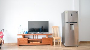 A modern living room with a flat-screen TV on a wooden entertainment unit, a stainless steel refrigerator, and a wooden chair. - 3BR bedroom house near the beach and golf course  (Da Nang)