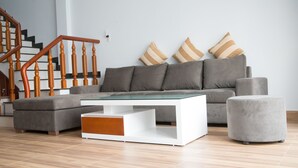 A modern living room with a grey sofa, striped cushions, a white coffee table, and a grey ottoman. - 3BR bedroom house near the beach and golf course  (Da Nang)