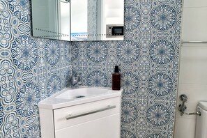 Un baño con pared de azulejos con diseño, un lavamanos blanco, un espejo y un inodoro.