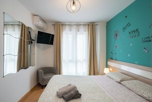 A hotel room with a bed, a chair, a TV, and a wall with a floral design.