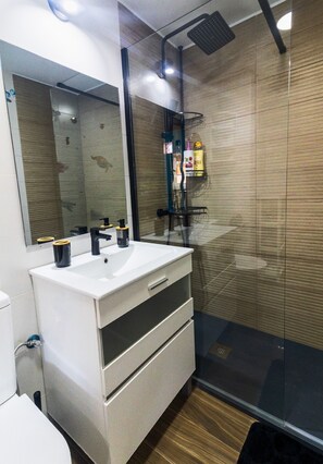 Un baño moderno con un lavabo blanco, grifo negro y cabina de ducha de vidrio.