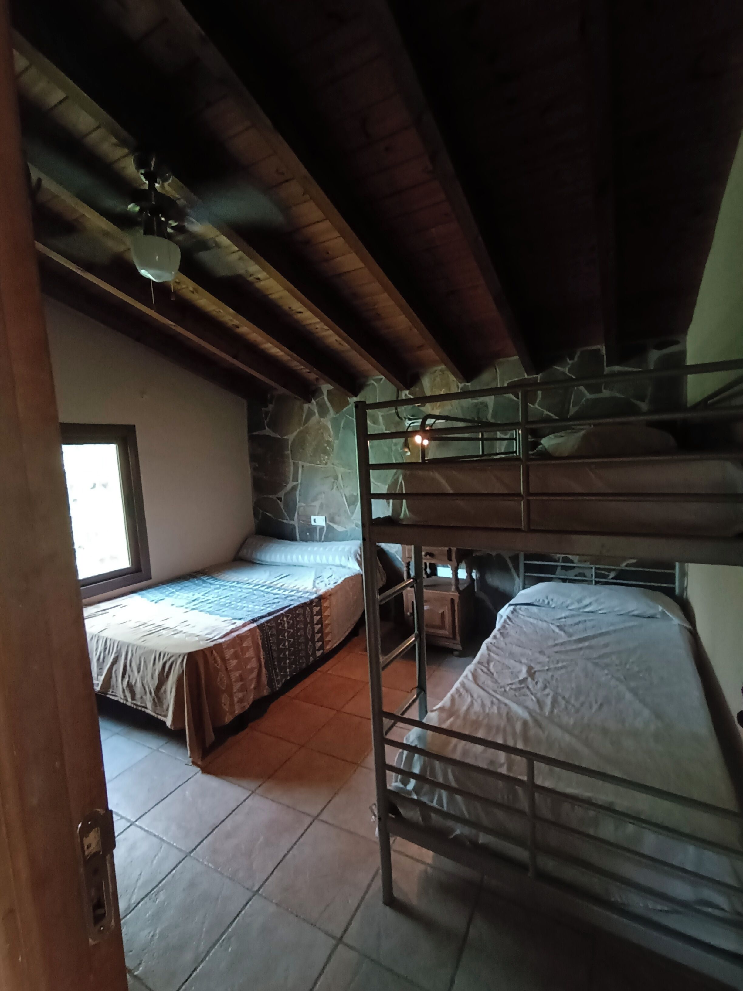 A room with bunk beds, a window, a stone wall, and a ceiling fan.