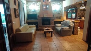 Ein Wohnzimmer mit Kamin, zwei Sofas, einem Couchtisch und einer Küchenzeile inklusive Herd und Pendelleuchten.