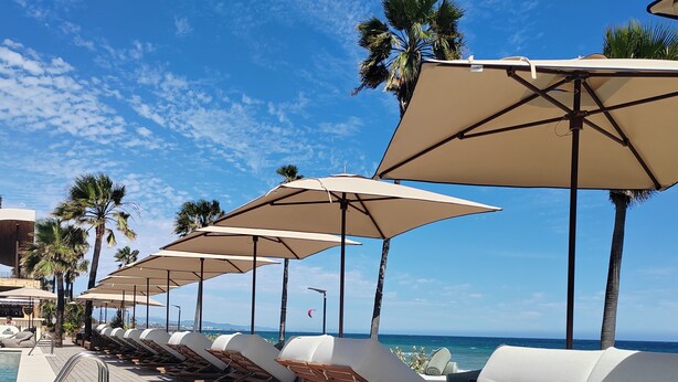Terraza con sillones y sombrillas, con vista a una piscina y al océano.