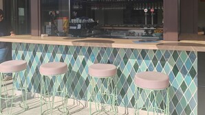 Un área de bar con salpicadero de azulejos, taburetes de metal verde y sombrillas naranjas colgantes.