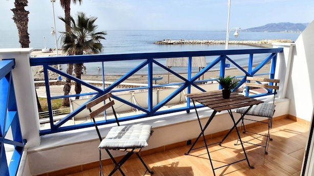 Un balcón con mesa y sillas de madera, con vistas a la playa y al mar.