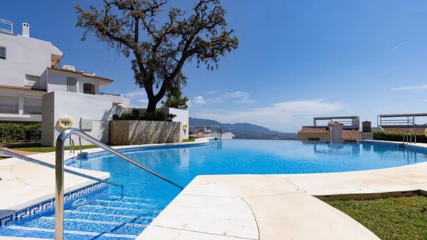 A swimming pool with a clear blue water, surrounded by a white building with a tree in the center. - Casa de Mairena - Sea/Mountain Views + Infinity Pool (Marbella)