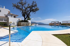 A swimming pool with a clear blue water, surrounded by a white building with a tree in the center.
