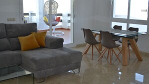 A modern living room with a grey sofa, a glass coffee table, and a dining area with a glass table and chairs. - Casa de Mairena - Sea/Mountain Views + Infinity Pool (Marbella)