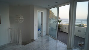 Ein geräumiger Balkon mit Blick auf das Meer, eine Glastür, die zu einem Raum führt, und ein weißes Geländer.