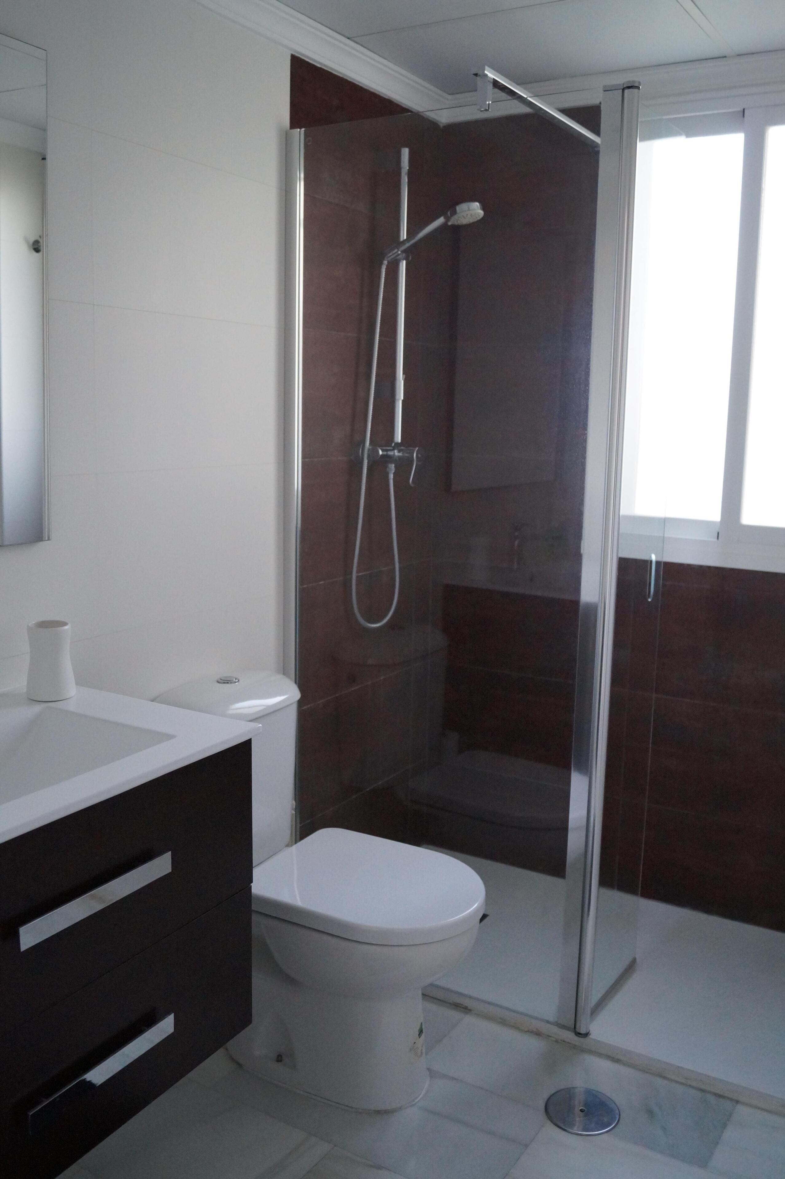 Ein modernes Badezimmer mit einer gläsernen Duschkabine, einer weißen Toilette und einem dunklen Waschtisch.