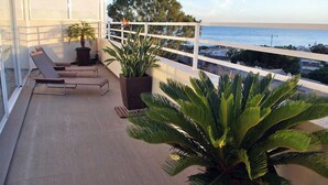 Ein Balkon mit Liegestühlen und Topfpflanzen mit Blick auf einen Strand.