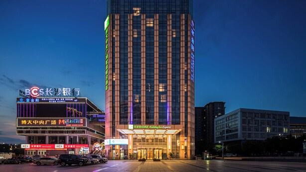 A Holiday Inn Express hotel with a modern glass facade, a prominent entrance, and a parking lot in front. - Holiday Inn Express Liuyang Development Zone by IHG (Changsha)