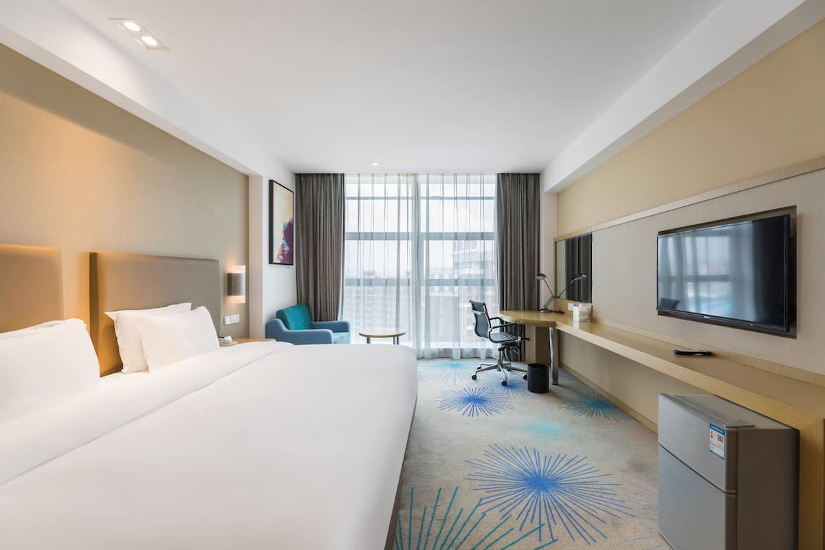 A hotel room with a large bed, a desk with a chair, a television, and a window with curtains.