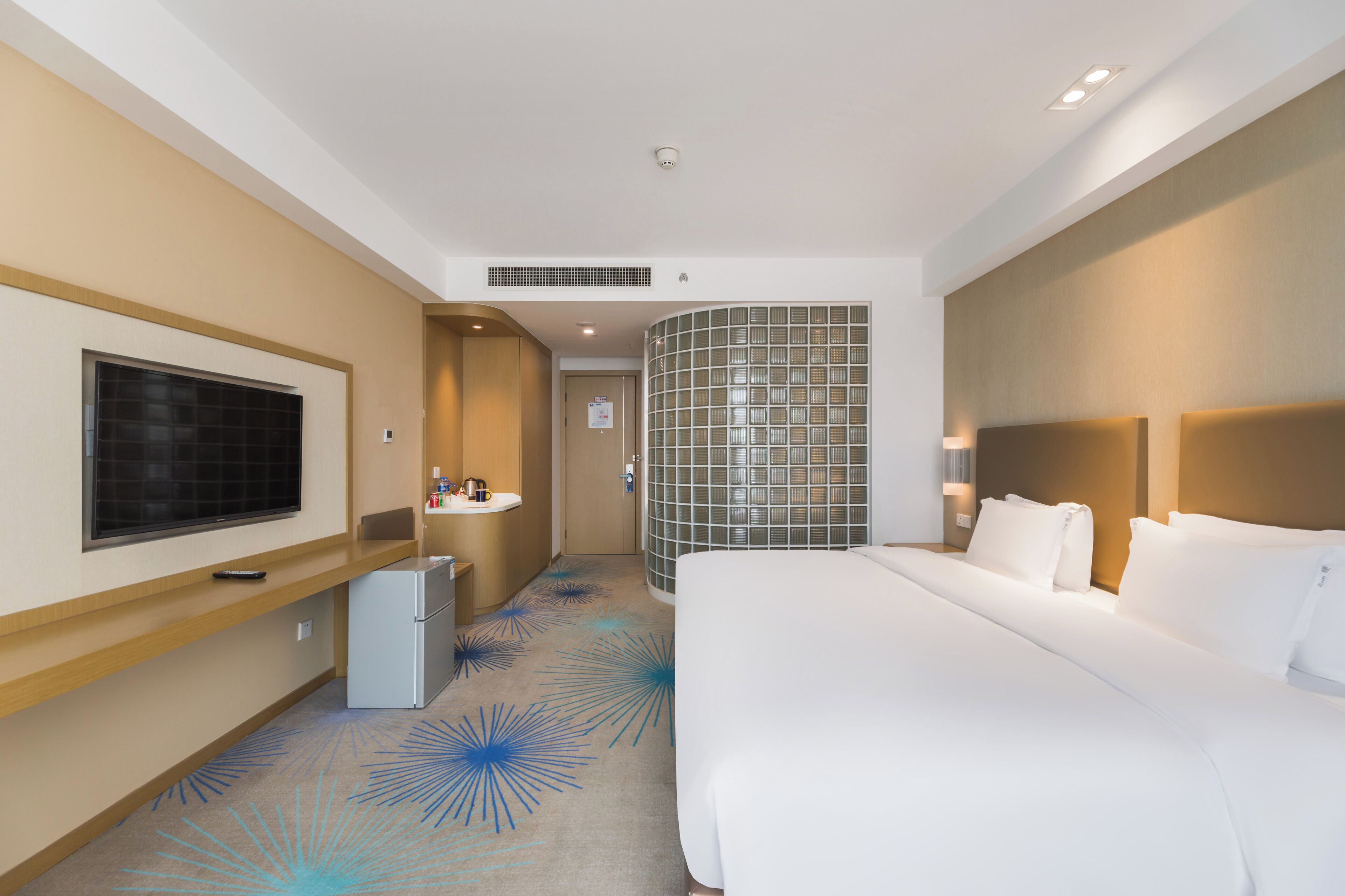 Une chambre d’hôtel avec un grand lit, une télévision, une petite kitchenette, une salle de bain et un mur décoratif.
