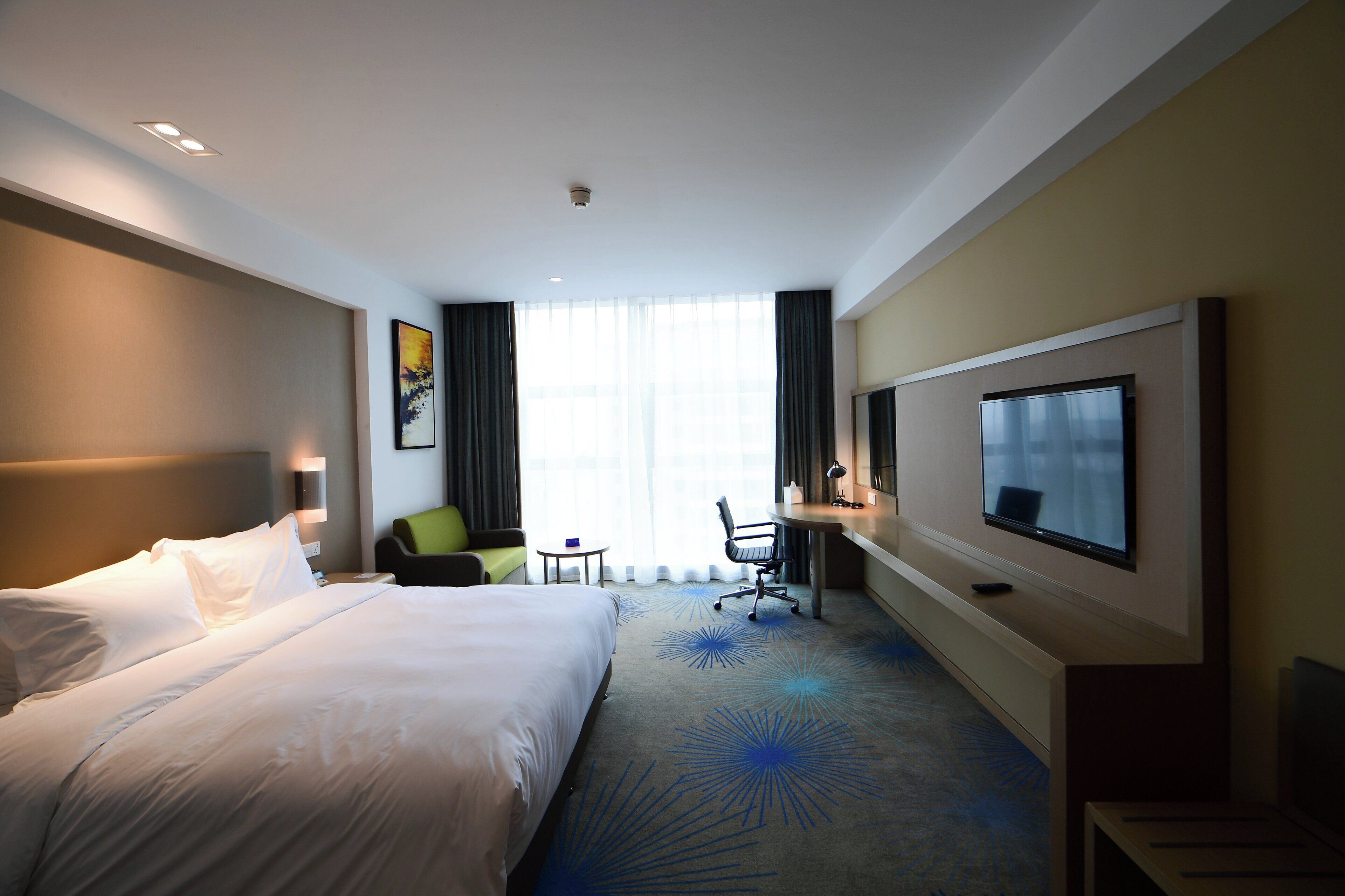 A hotel room with a large bed, a desk with a chair, a television, and a window with curtains.