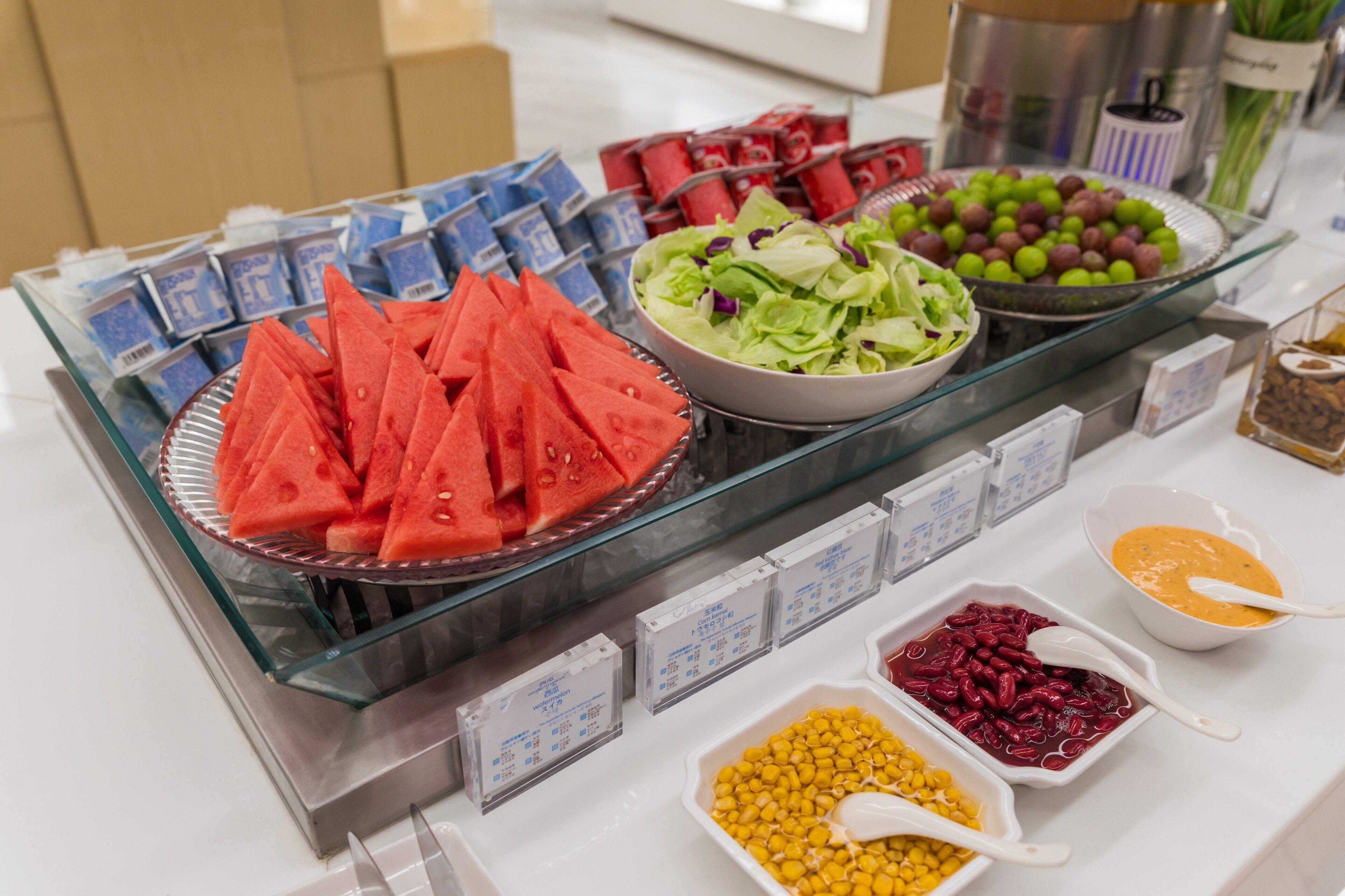 Un bufé con diversos alimentos, incluyendo sandía, uvas, maíz y una ensalada.
