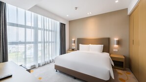 A modern hotel room with a large bed, bedside tables, a desk, and a view of the city through large windows. - Holiday Inn Express Liuyang Development Zone by IHG (Changsha)