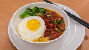 A bowl of ramen with a fried egg, broccoli, and red vegetables on a white plate. - Holiday Inn Express Liuyang Development Zone by IHG (Changsha)