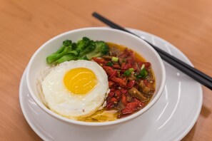 A bowl of ramen with a fried egg, broccoli, and red vegetables on a white plate.
