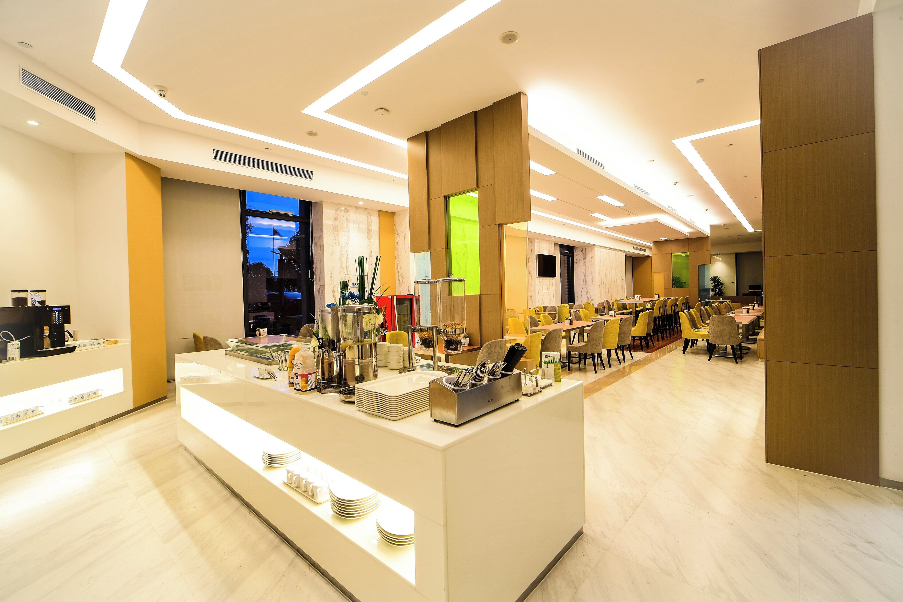A modern hotel lobby with a reception desk, seating area, and a view of the cityscape through the windows.